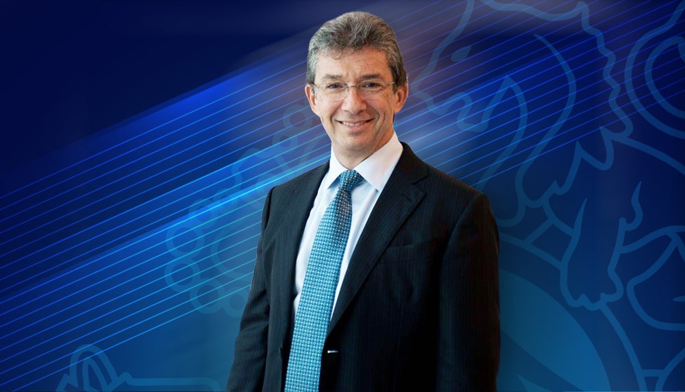 Andre Calantzopoulos smiling in a white shirt, blue tie, and a black formal coat.